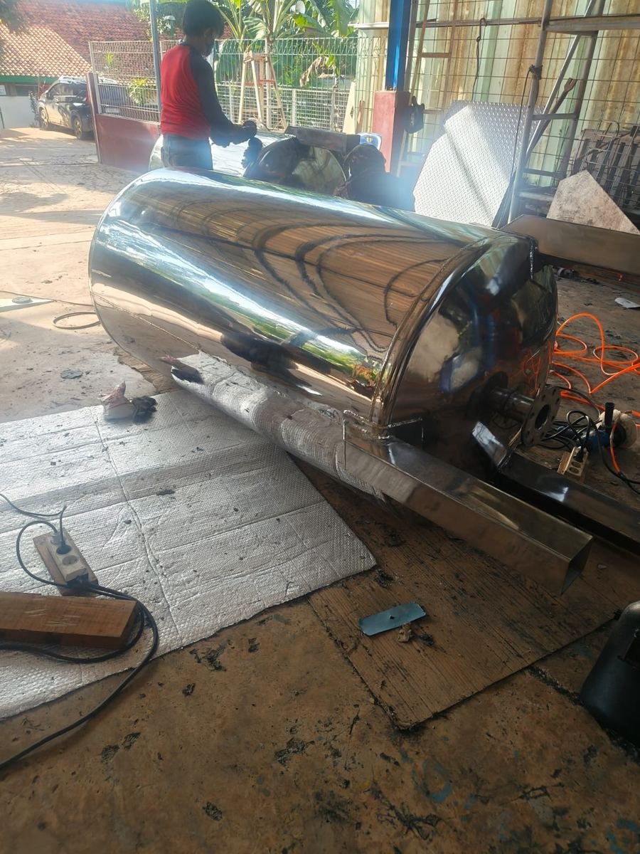 Pekerja mengerjakan bodi tangki stainless steel yang mengilap di area workshop