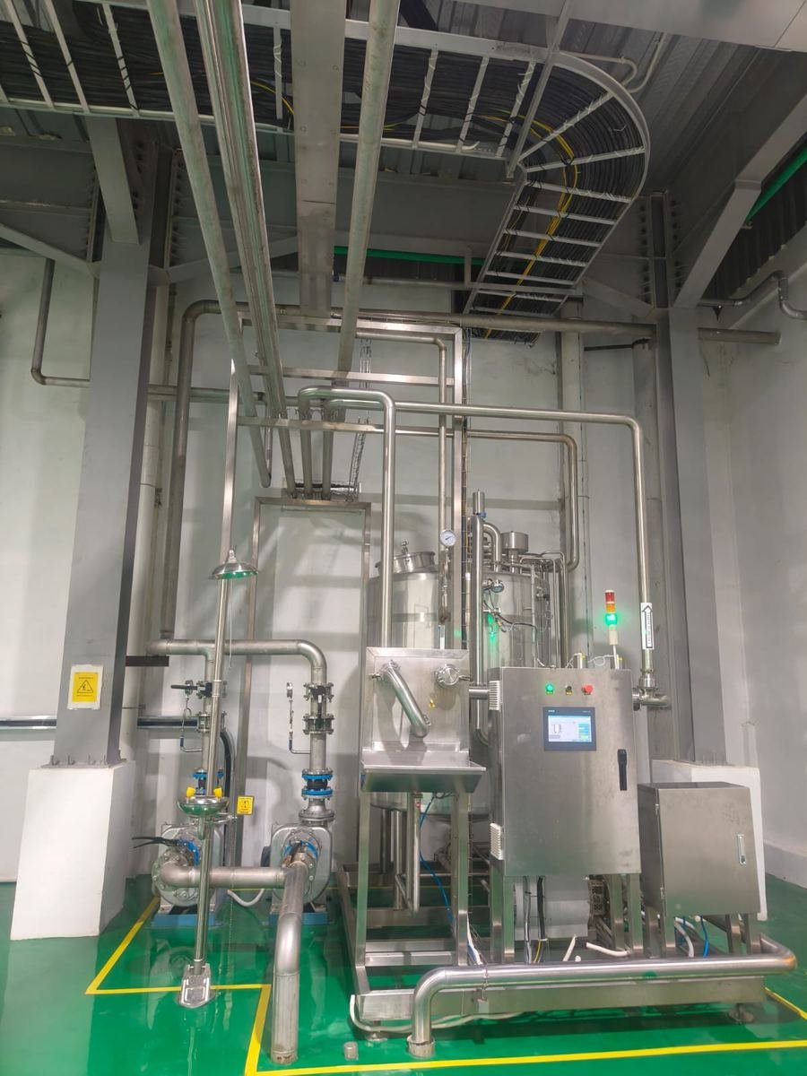 Instalasi piping stainless steel dan panel kontrol layar sentuh di ruang produksi berlantai epoksi hijau
